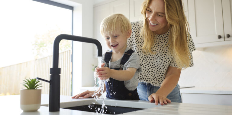 Mother With Son At Home In Kitchen Washing Hands In Sink Or Basin Together
